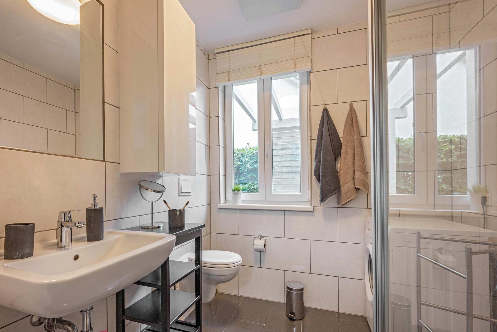 Badezimmer mit Waschbecken, Toilette, Dusche und Fenster.