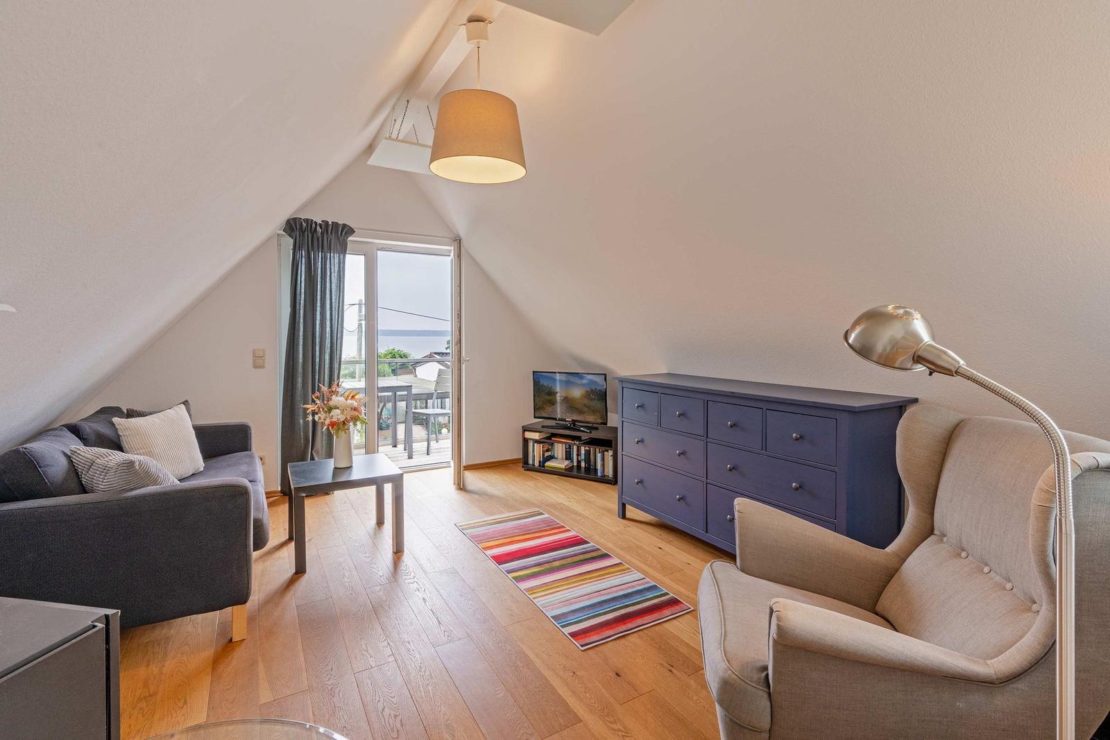 Wohnzimmer mit Sofa, Sessel, TV und Balkonzugang.