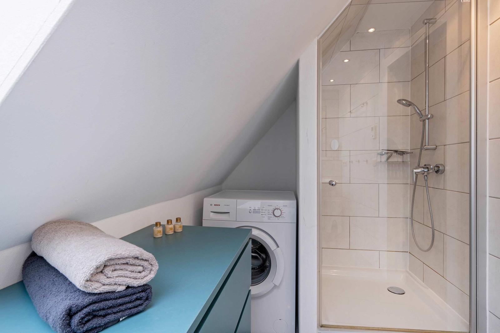 Duschbereich mit Dusche und Waschmaschine unter Dachschräge