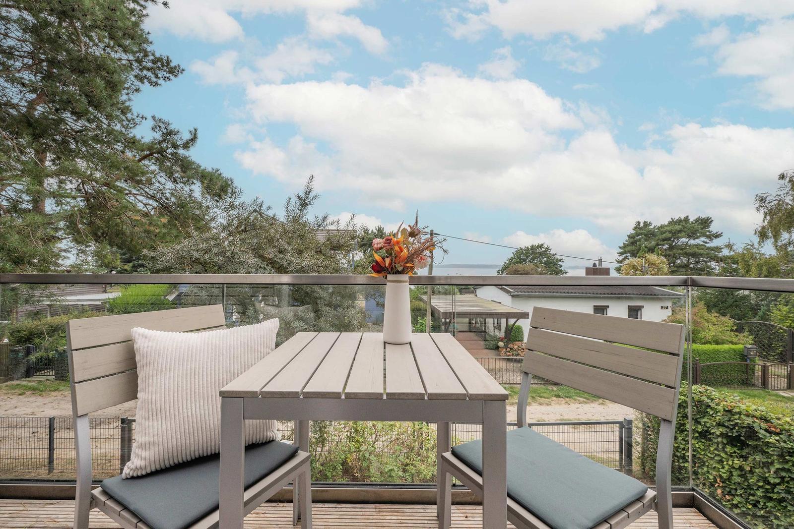 Terrasse mit Tisch und zwei Stühlen, Blick auf Grün und Himmel.