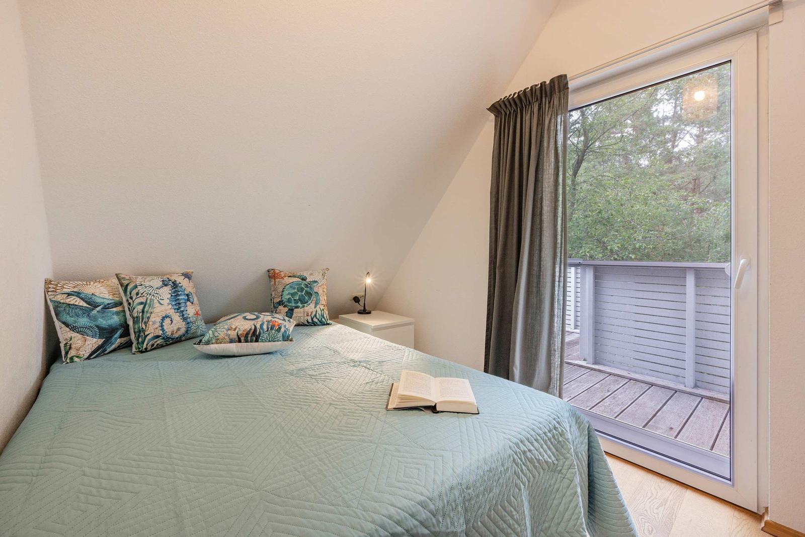 Schlafzimmer mit Bett, Kissen und Balkon. Blick auf grüne Bäume.