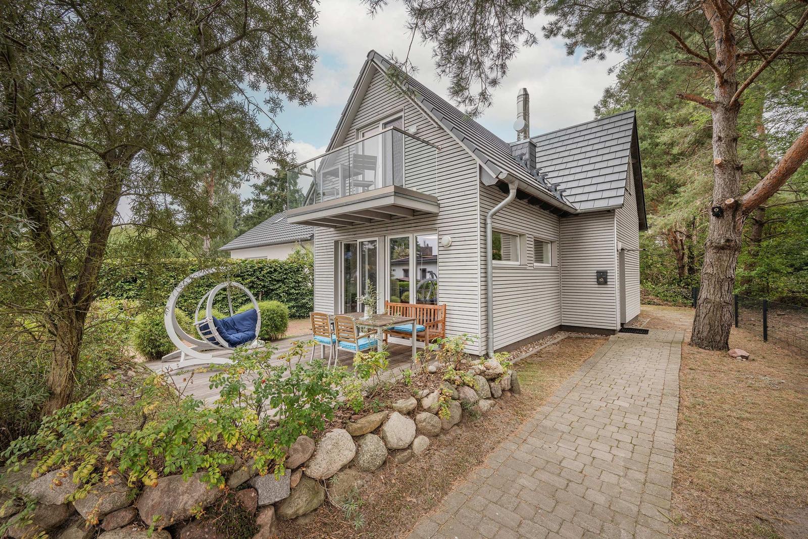 Moderne Villa mit Balkon, Terrasse und Garten. Holz- und Steinbeete umgeben das Haus.