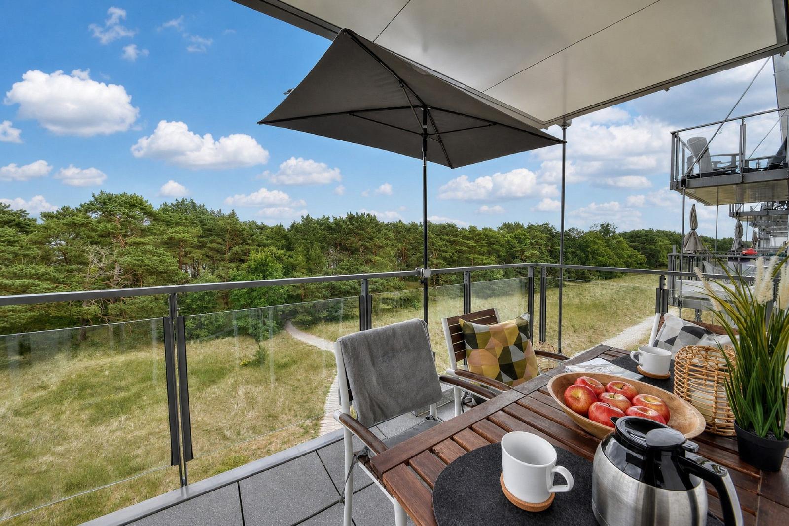 Terrasse mit Tisch, Stühlen und Sonnenschirm. Blick auf Wald und Himmel.