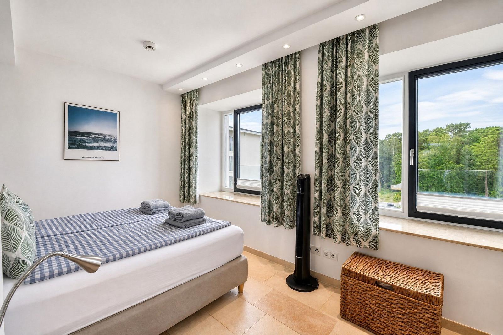 Schlafzimmer mit Bett, Fenster und Vorhängen. Blick auf grüne Landschaft.