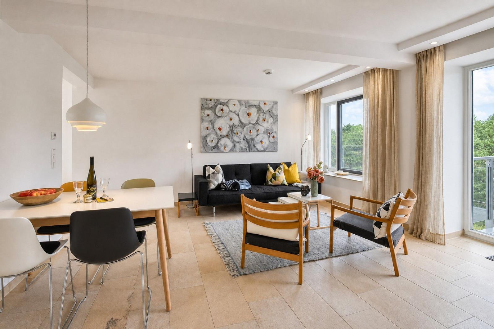 Wohn- und Essbereich mit Sofa, Stühlen und Fenstern mit Blick auf Grün.