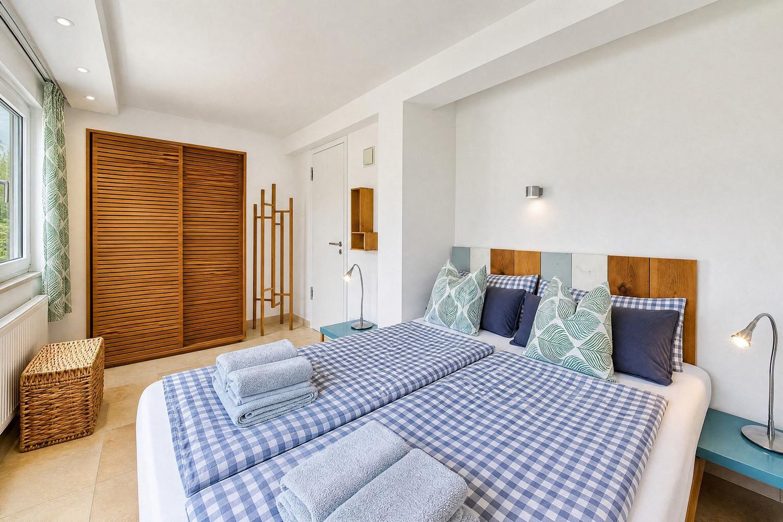 Schlafzimmer mit Doppelbett, Holzgarderobe und Fenster mit Vorhängen.