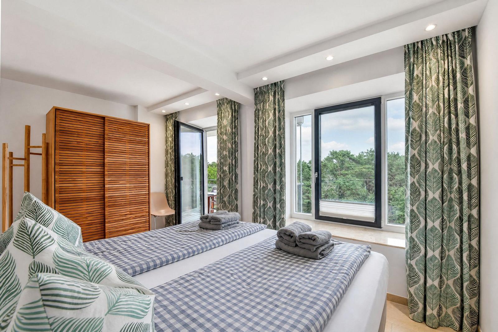 Schlafzimmer mit Doppelbett, Holzschrank und Fensterblick auf Wald.