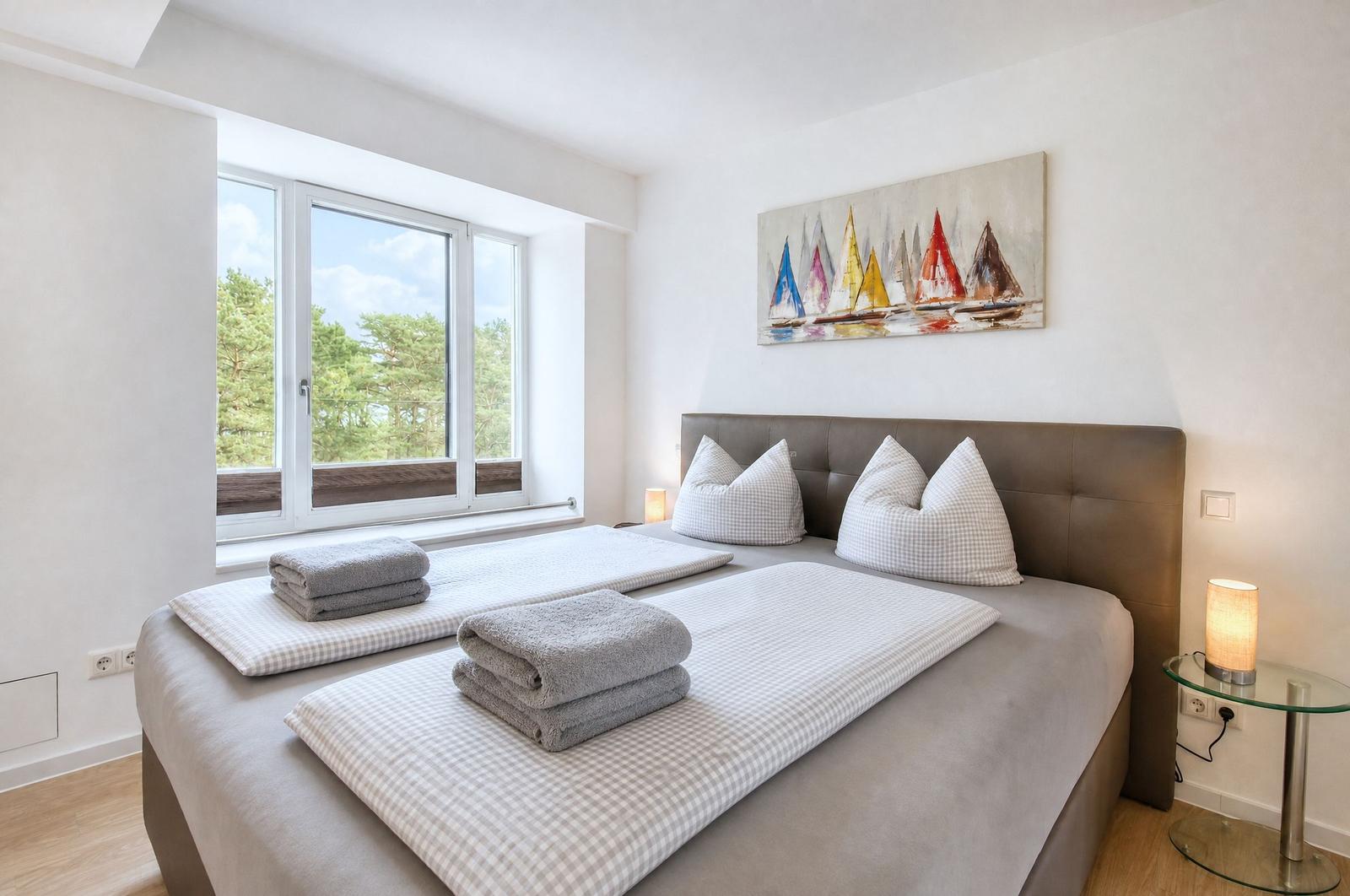 Schlafzimmer mit Doppelbett, Fensterblick auf Bäume und Wandbild mit Segelbooten.