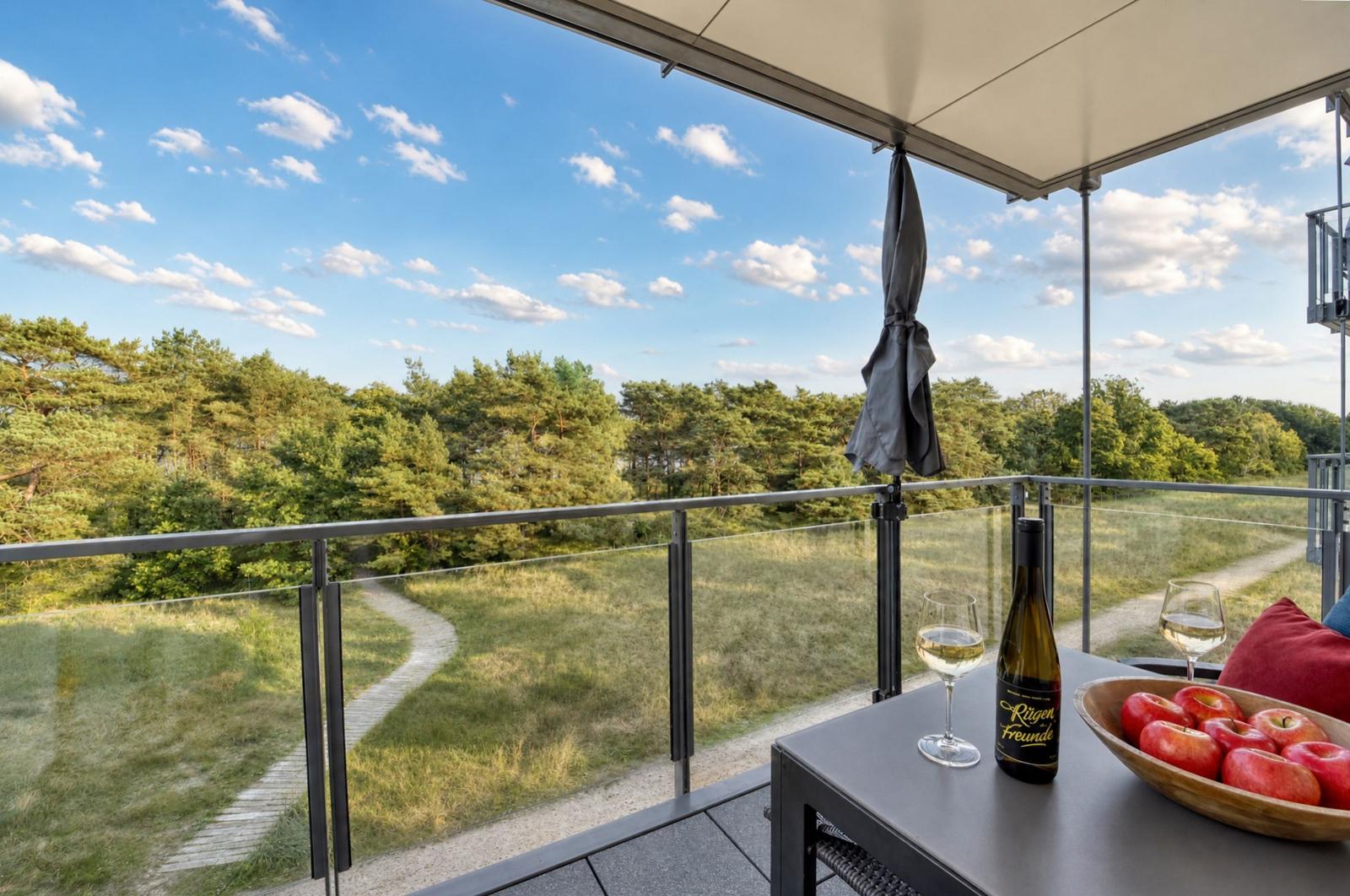 Terrasse mit Blick auf Wald, Tisch mit Wein und Äpfeln, Sonnenschutz und Glasgeländer.
