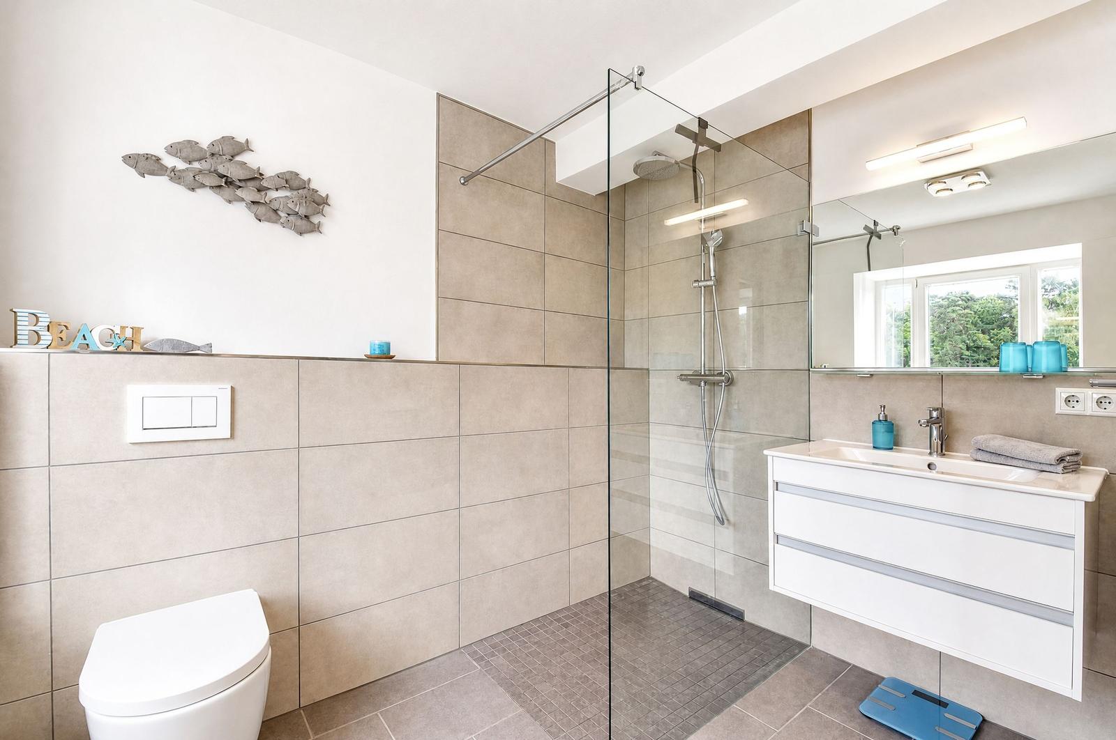 Badezimmer mit Dusche, Waschbecken und Toilette. Wanddekoration mit Fischen.