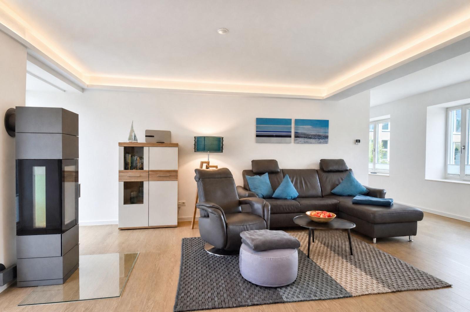 Wohnzimmer mit Sofa, Sessel und Kamin. Holzboden und Wandbilder sichtbar.