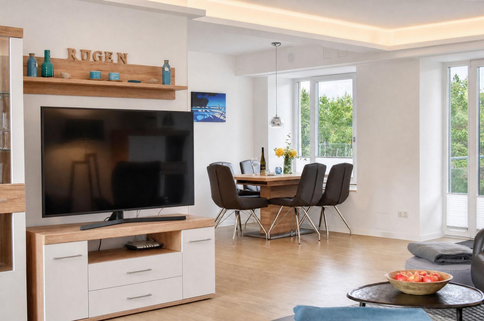 Wohn- und Essbereich mit TV, Esstisch und Blick auf Balkon.