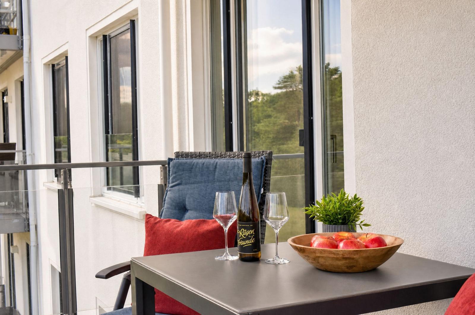 Terrasse mit Tisch, Stühlen, Weinflasche und Obstschale.