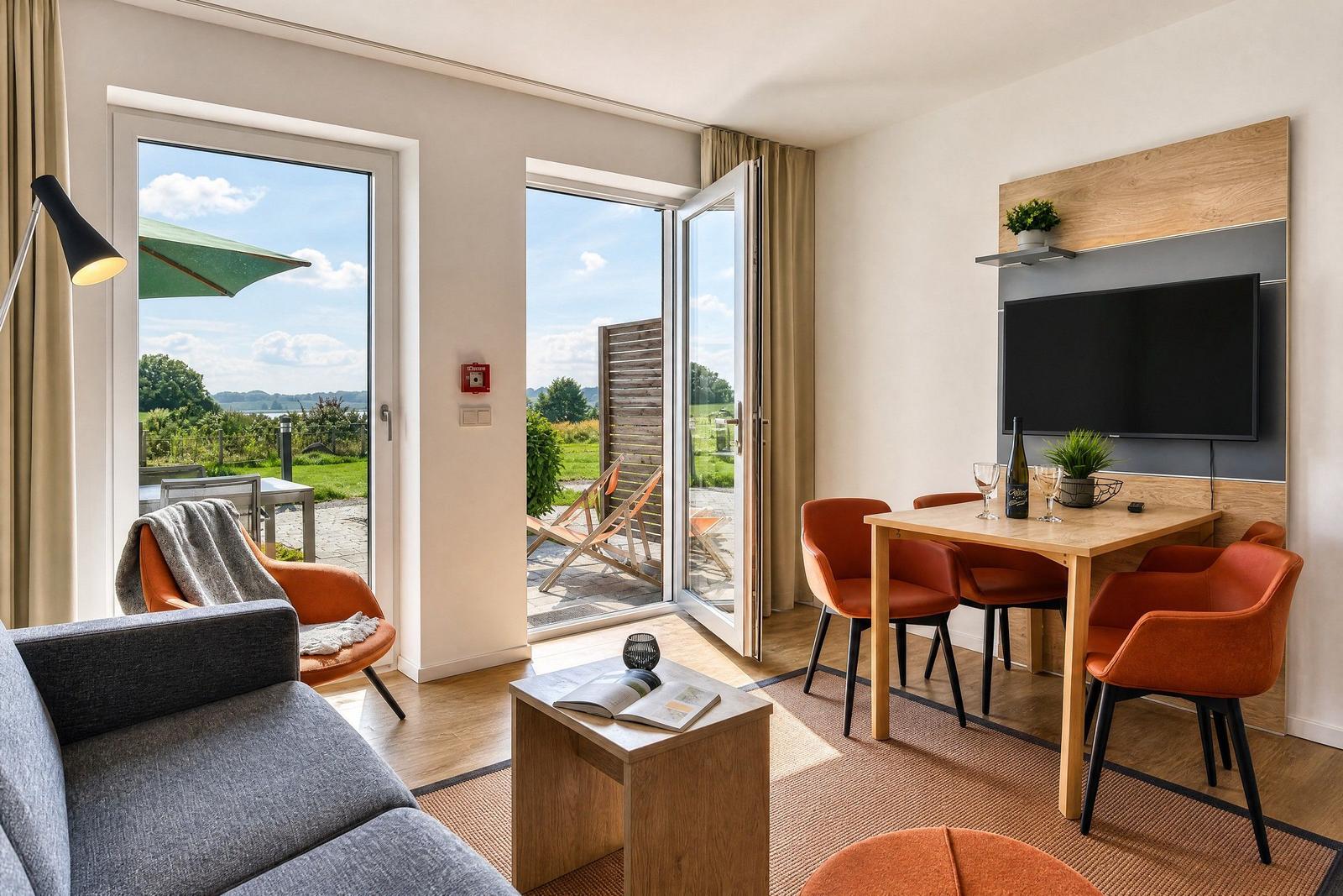 Wohnbereich mit Essplatz, TV und Blick auf Garten. Orange Sitzmöbel und Holzmöbel.