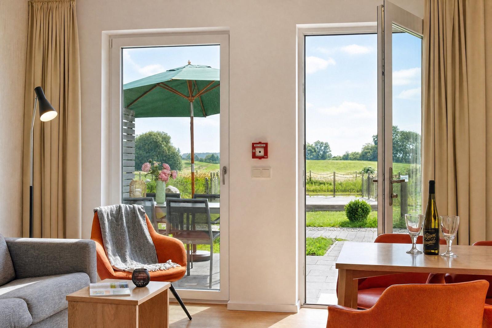 Wohnraum mit Sitzgelegenheiten und Blick auf Garten mit Sonnenschirm.