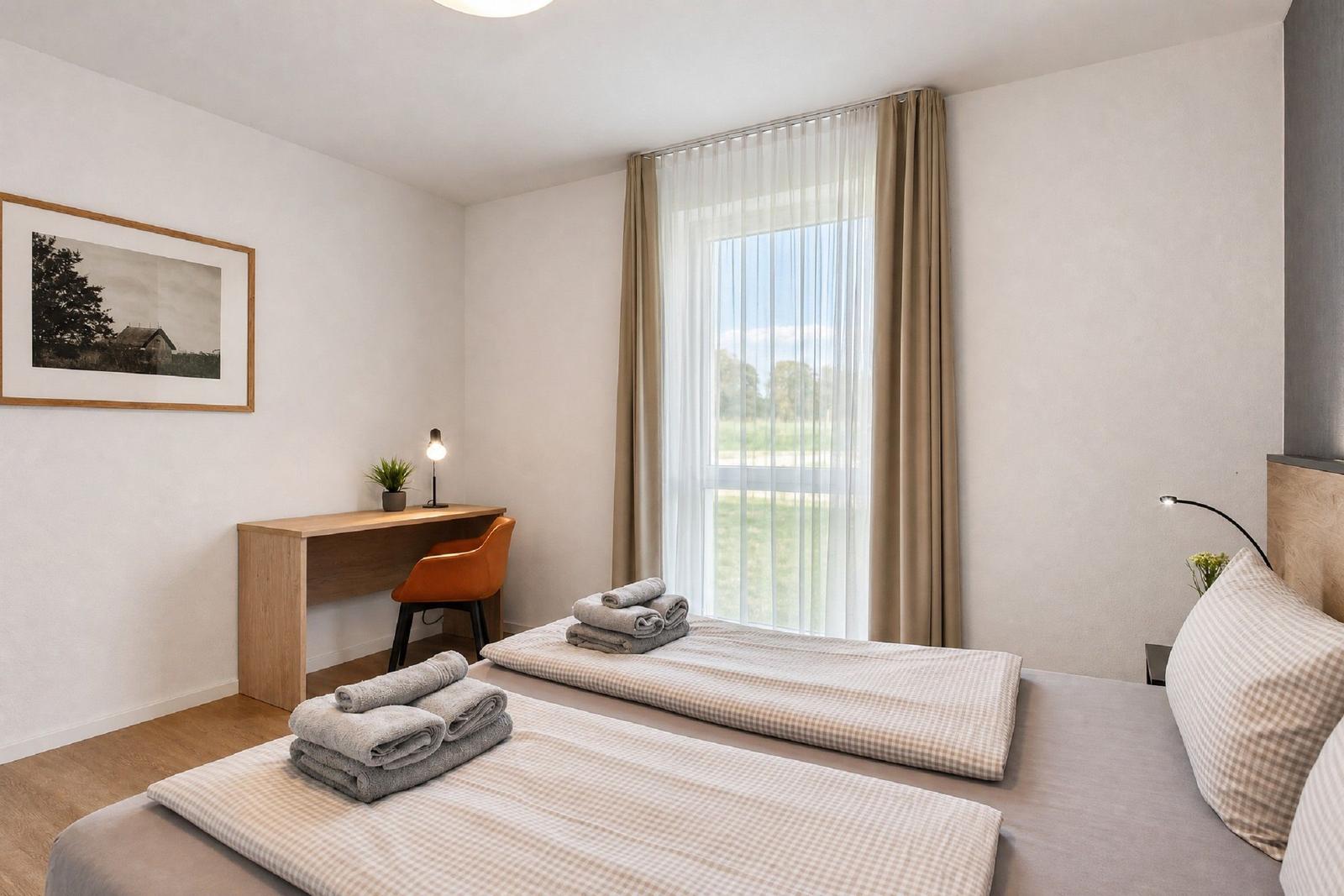 Zimmer mit zwei Betten, Schreibtisch und Fenster mit Blick auf Grünfläche.