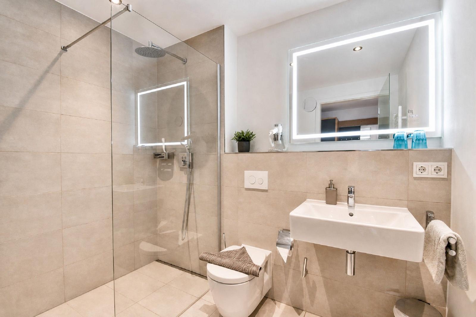 Bad mit Dusche, Waschbecken und Toilette. Spiegel mit Beleuchtung und Handtuchhalter.