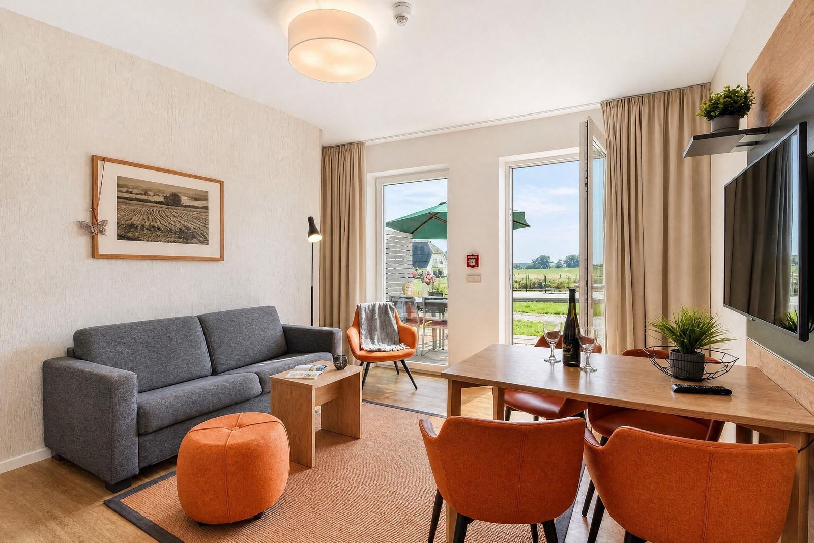 Wohn- und Essbereich mit Sofa, Tisch und Stühlen. Durchgang zur Terrasse mit Blick auf Felder.