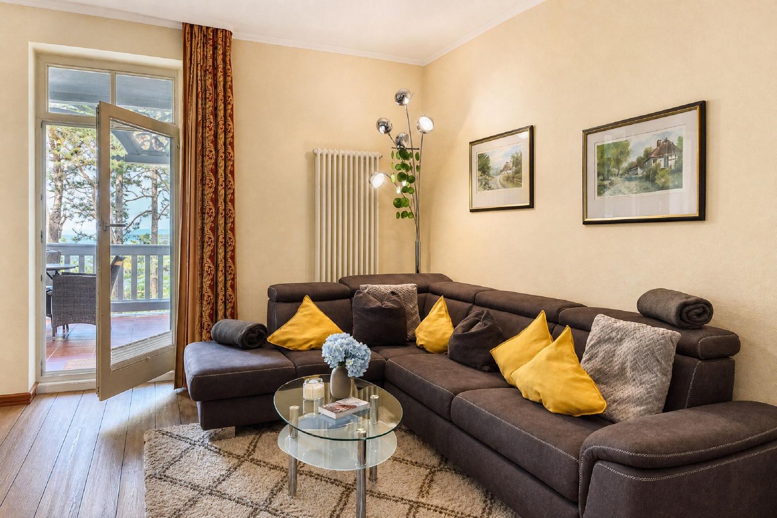 Wohnzimmer mit braunem Sofa, gelben Kissen und Blick auf Balkon