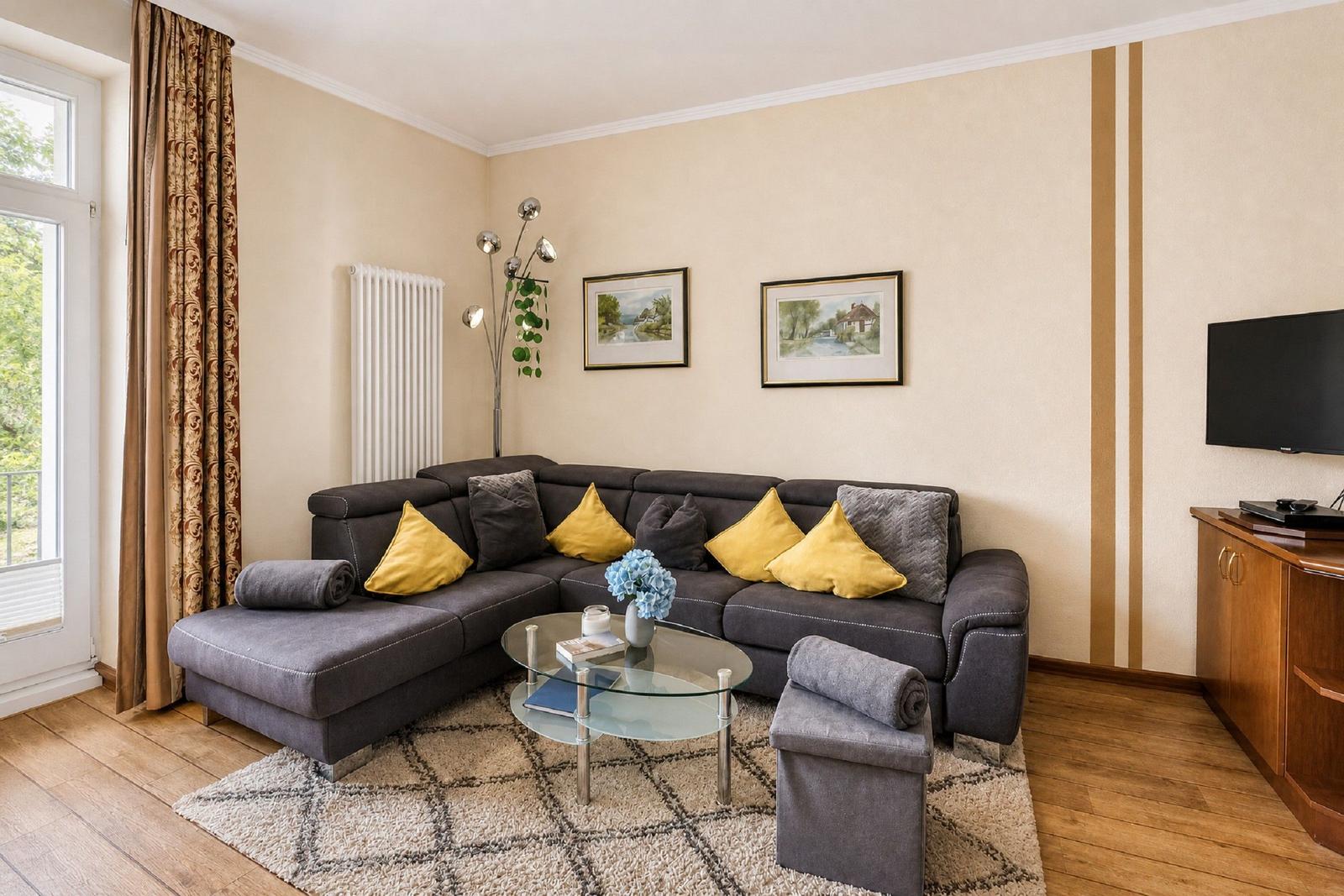 Ein Wohnzimmer mit grauem Sofa, gelben Kissen und Glas-Tisch.
