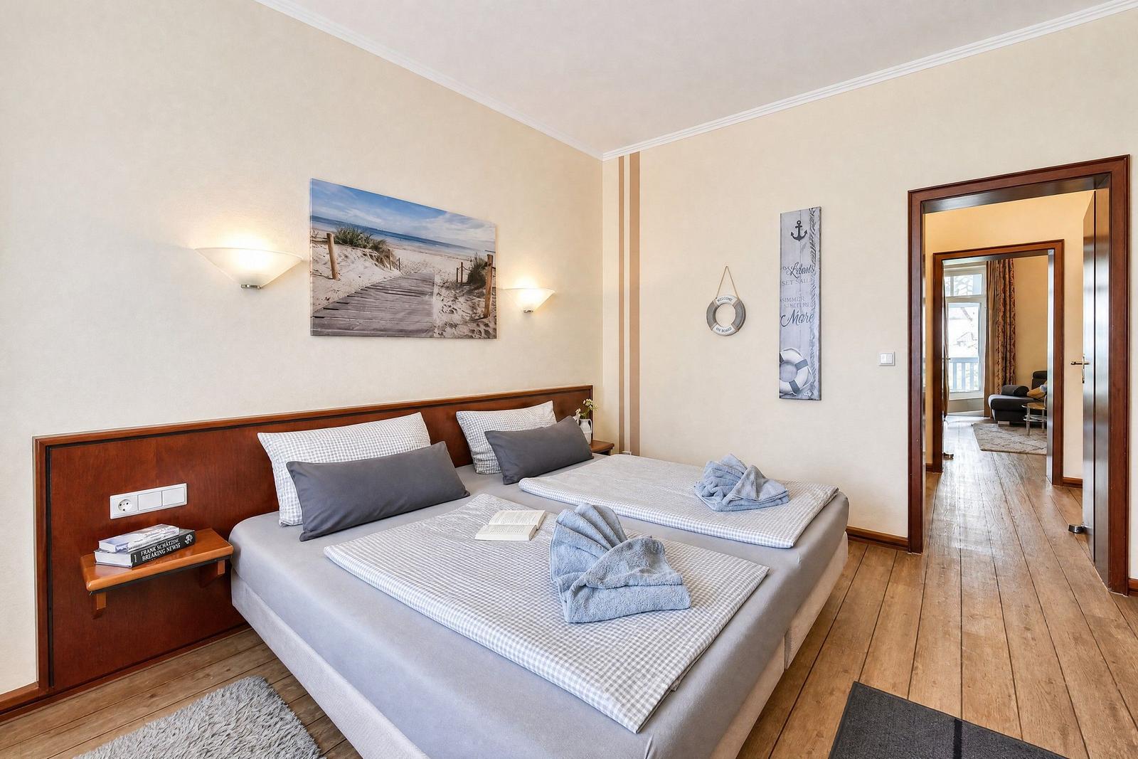 Schlafzimmer mit Doppelbett, Wandbild und Holzboden. Durchgang zu Wohnbereich.