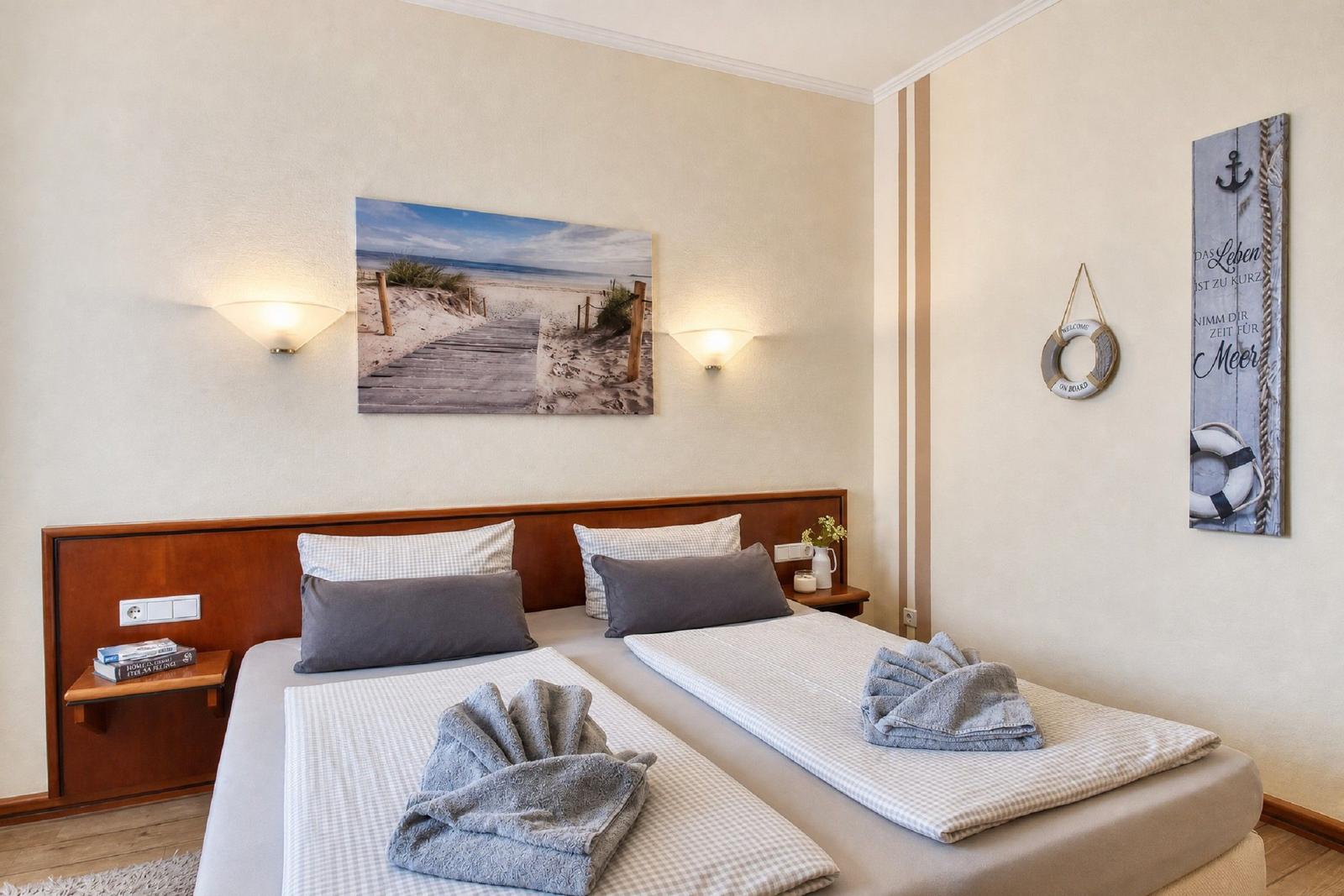 Zimmer mit Doppelbett, Strandbild, Nachttisch und maritimen Wanddekoration.