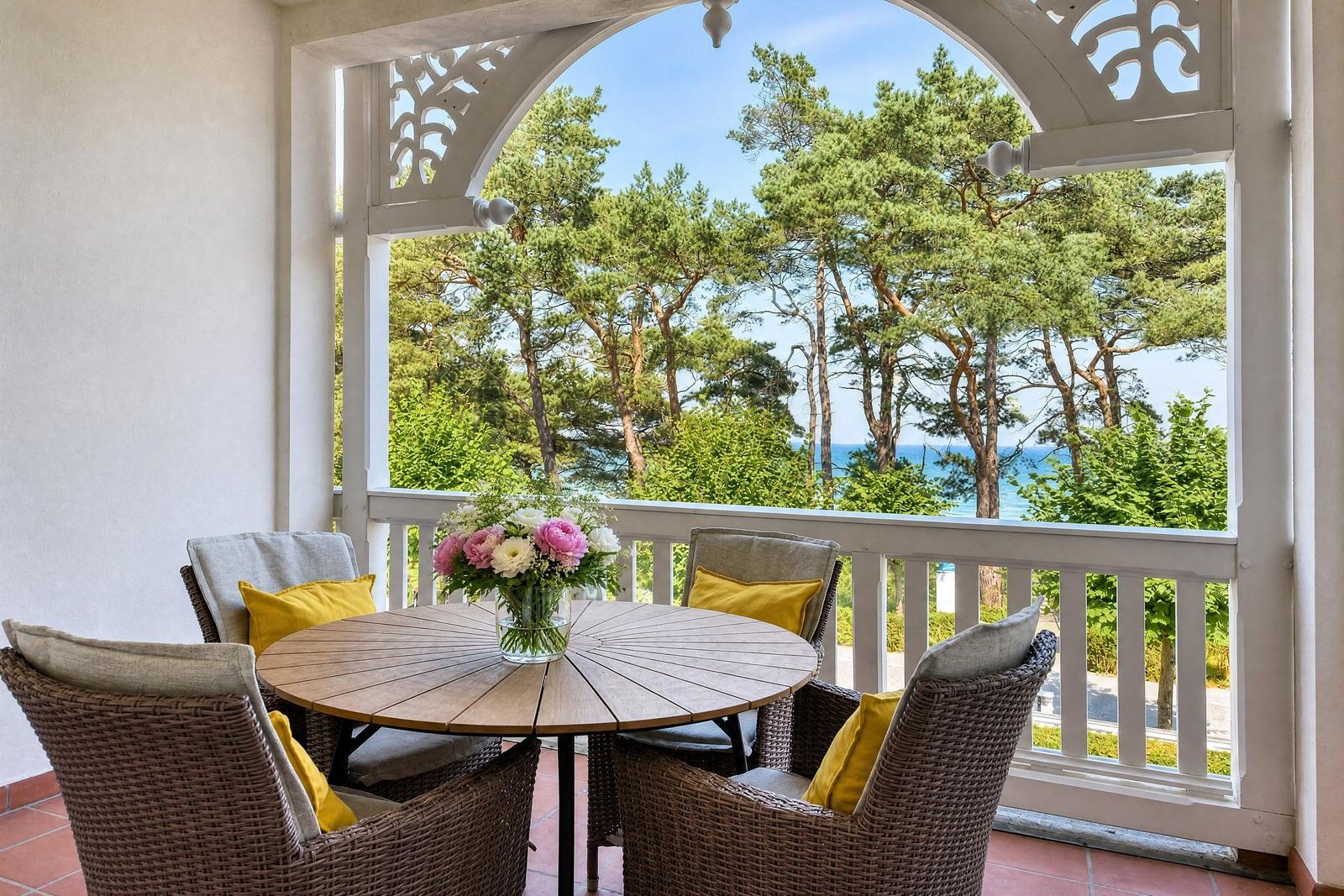 Terrasse mit runden Tisch und Stühlen, Blick auf Bäume und Meer.