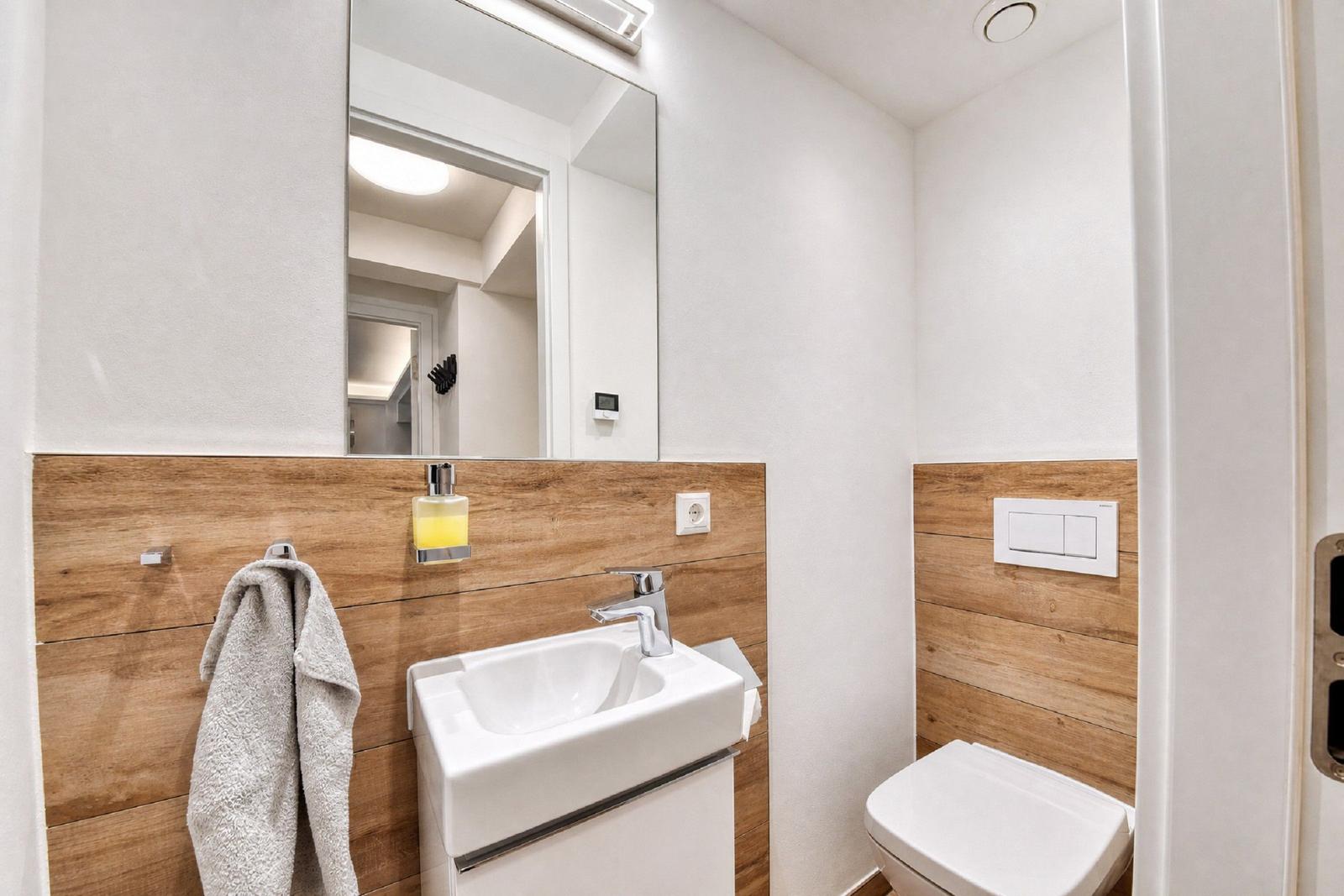 Badezimmer mit Waschbecken, Spiegel und Toilette. Holzwand und graue Handtuch.