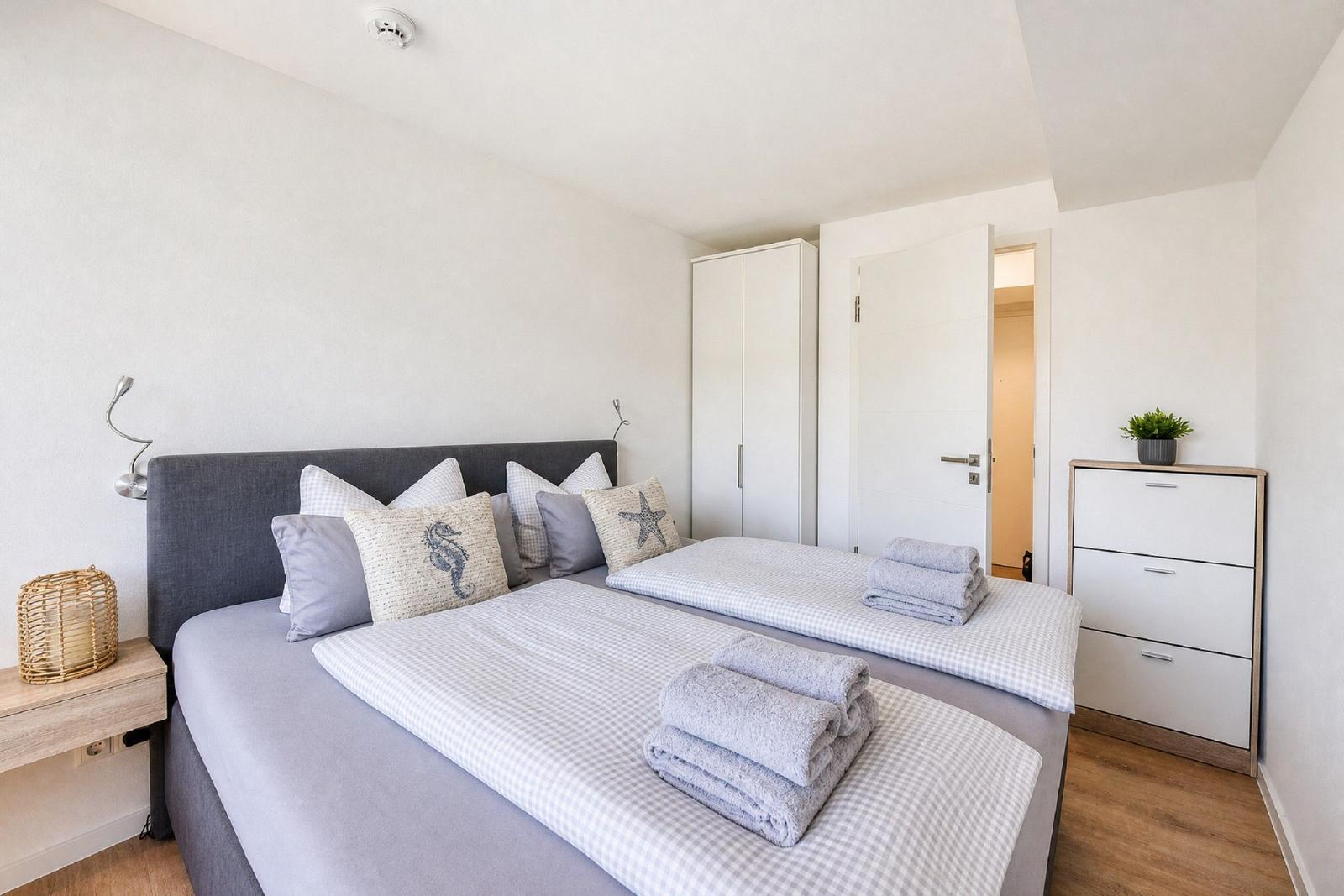 Schlafzimmer mit Doppelbett, Kissen, Handtüchern, Kleiderschrank und Nachttisch.