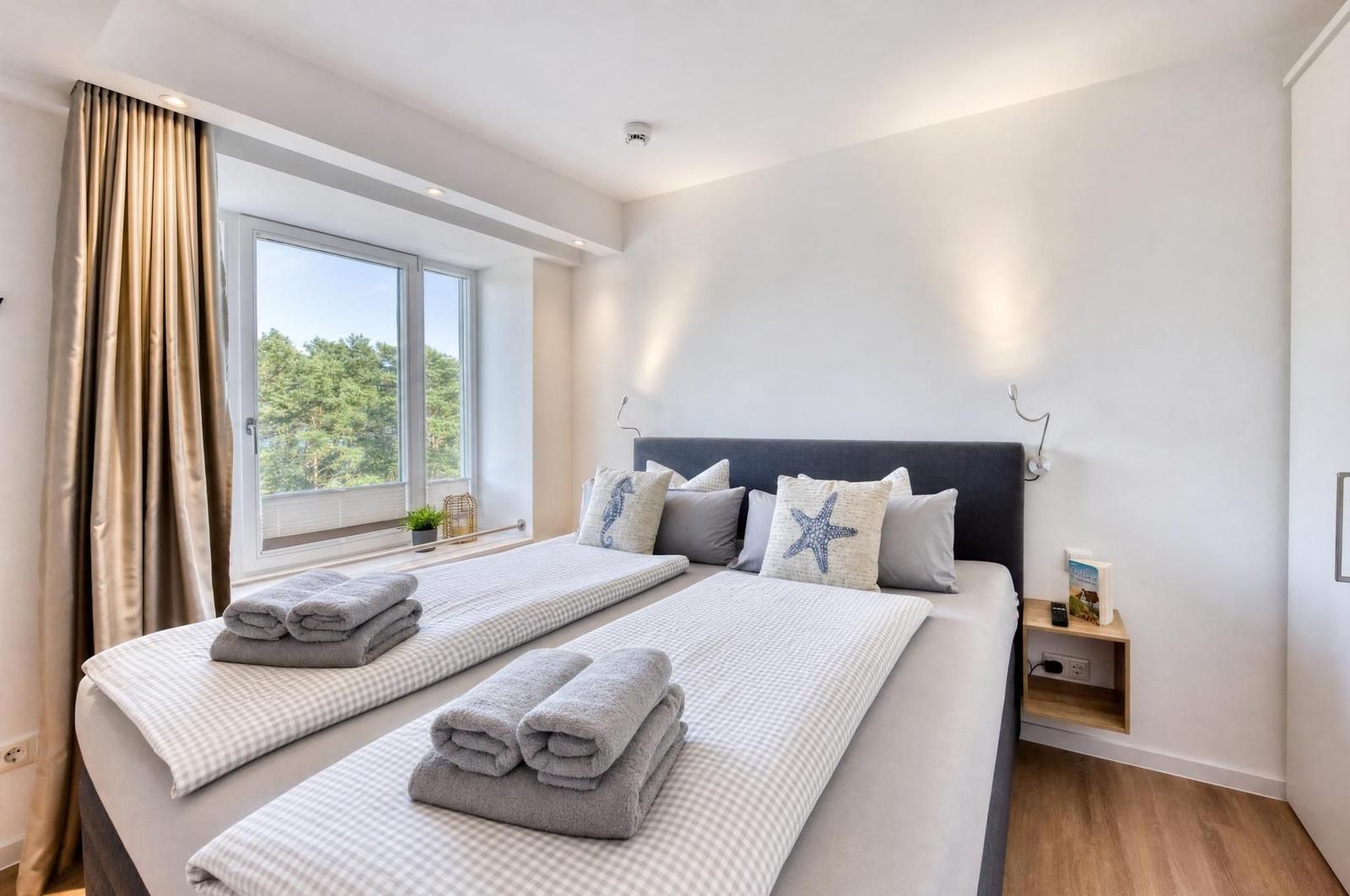 Schlafzimmer mit Doppelbett, Fensterblick auf Wald und gefalteten Handtüchern.