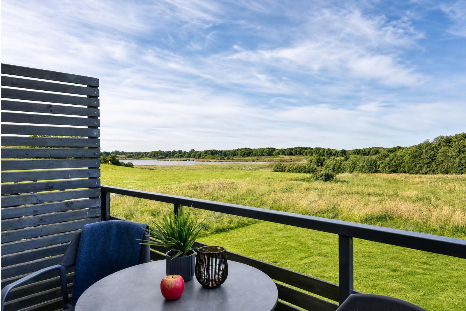 Terrasse mit Tisch, Stuhl und Blick auf Grünfläche und Wasser.