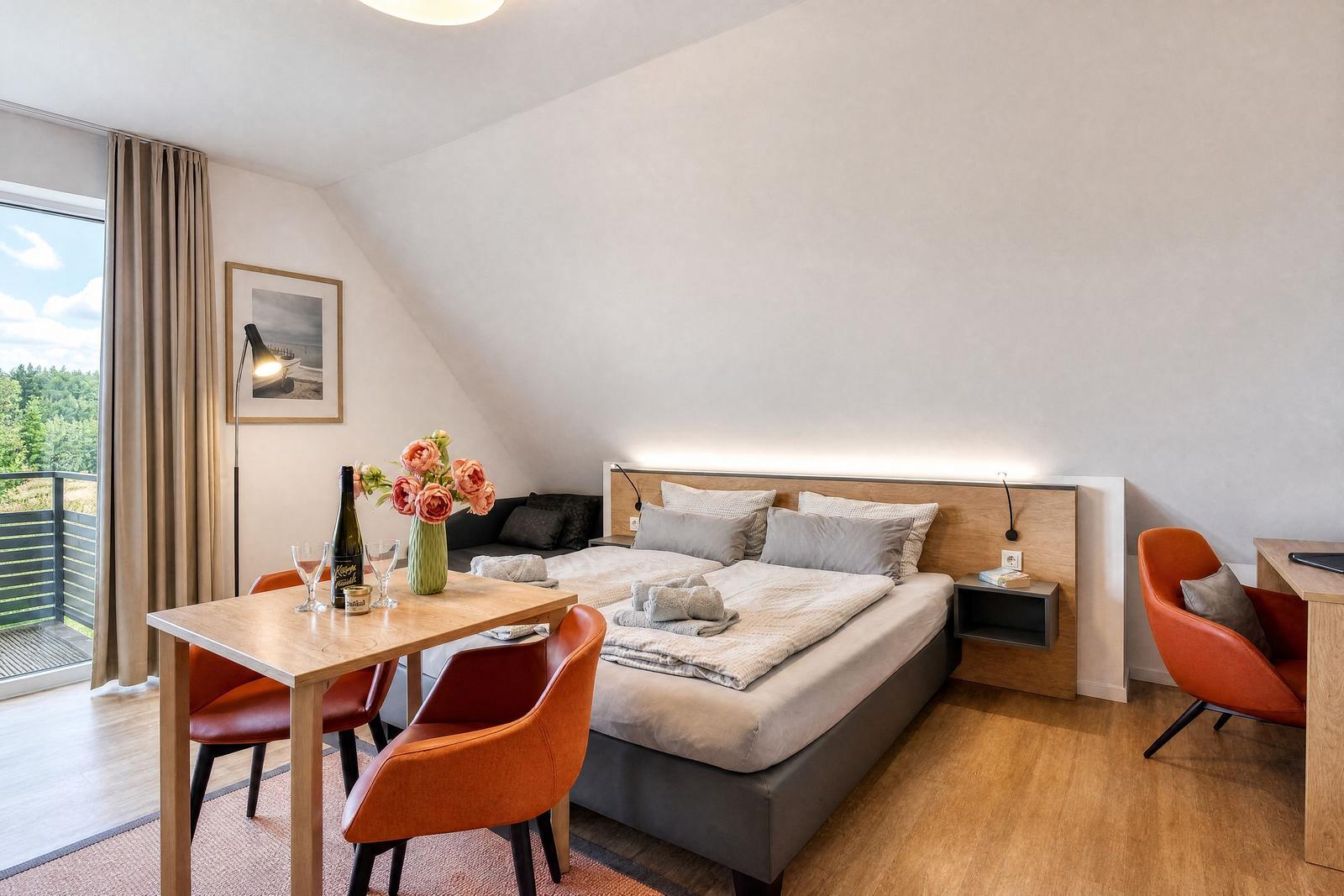 Doppelbett mit Nachttischen, Esstisch mit Stühlen und Balkon mit Blick auf Wald.