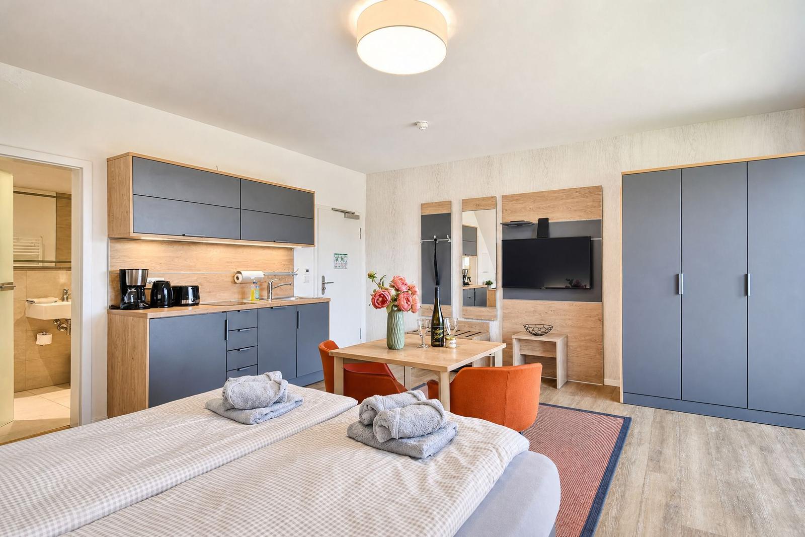 Ein Schlafzimmer mit Küchenzeile, TV und Bad. Ein Bett mit Handtüchern.