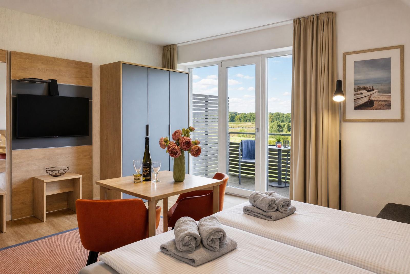 Zimmer mit zwei Betten, Tisch, Stühlen und Balkonblick.