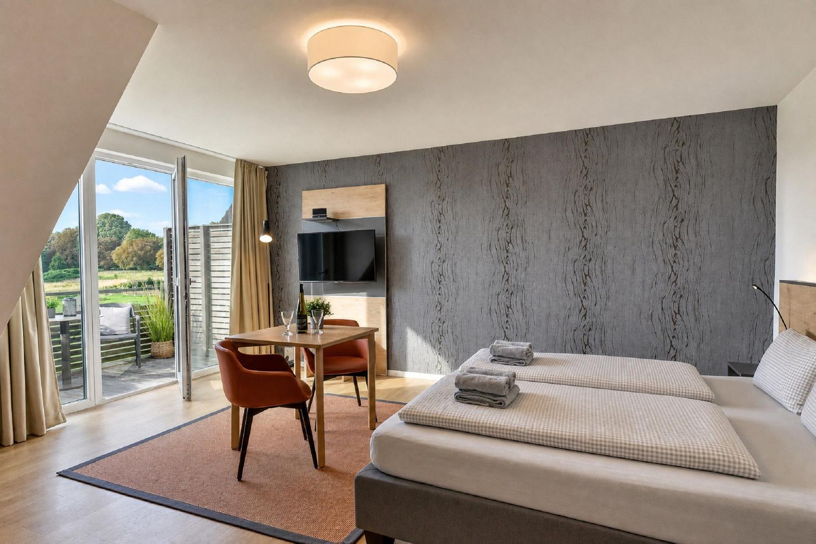 Bedroom with double bed, TV, and balcony view. Wooden floor and gray wall cladding.