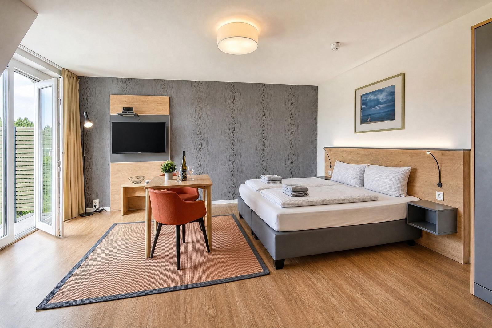A bedroom with a double bed, dining table, TV, and balcony door.
