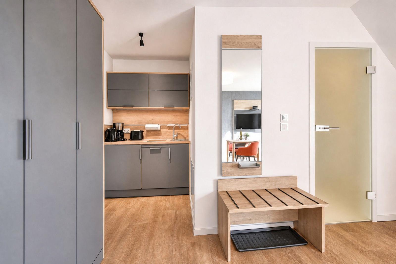 Kitchen with cabinets, sink, and appliances. Mirror, bench, and door are visible.