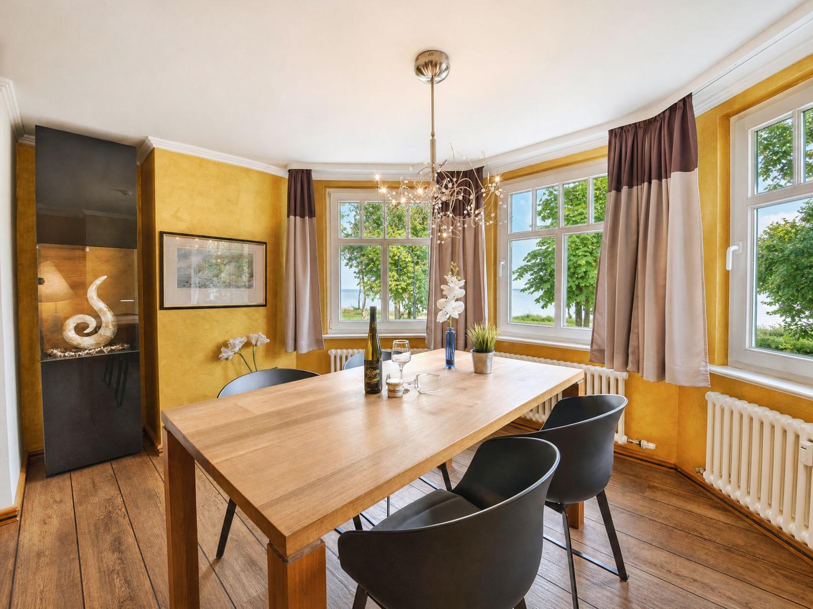 Esszimmer mit Holztisch, schwarzen Stühlen und Blick auf Wasser durch Fenster.
