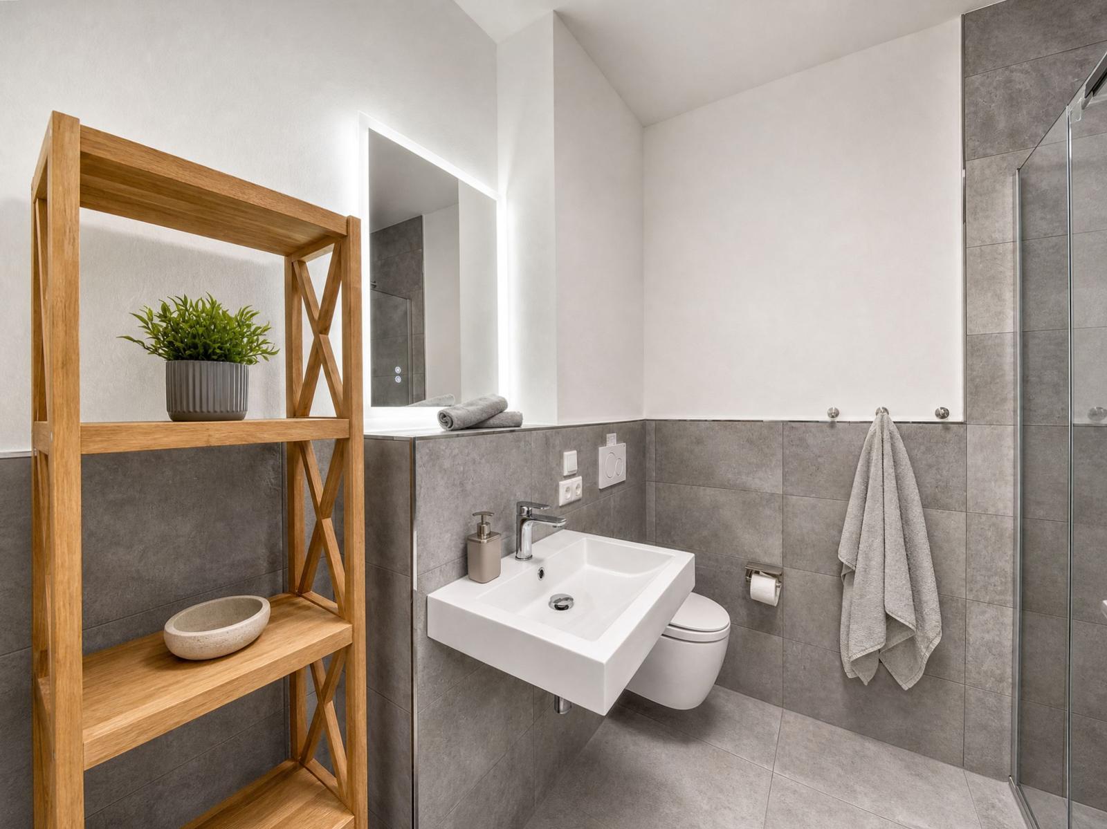 Bathroom with sink, toilet, and shower. Wooden shelf with plant and bowl.