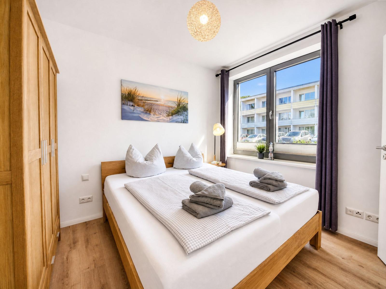Bedroom with wooden bed, wardrobe, and window view of buildings.