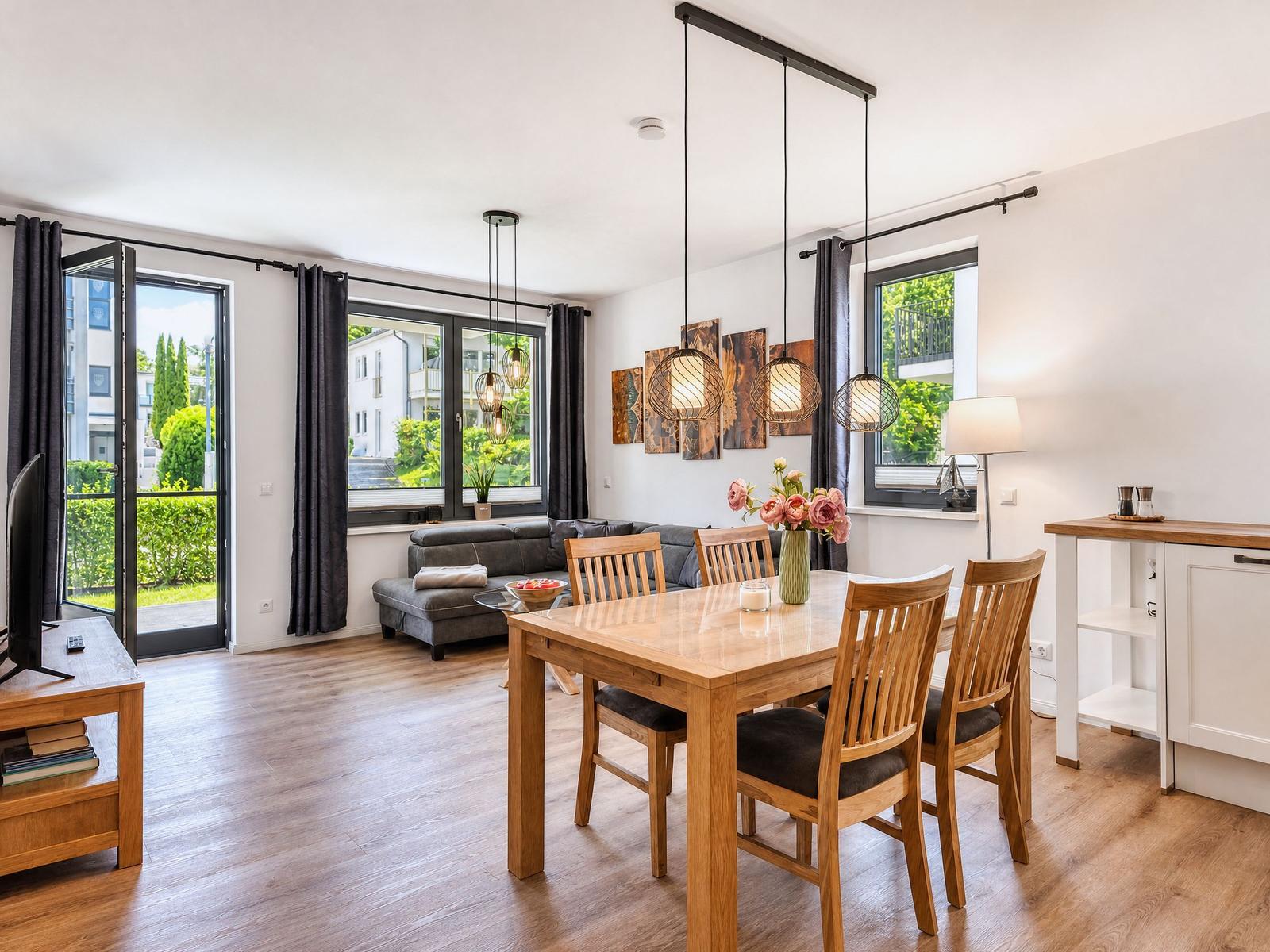 Dining area with wooden table and chairs, living area with sofa and windows.