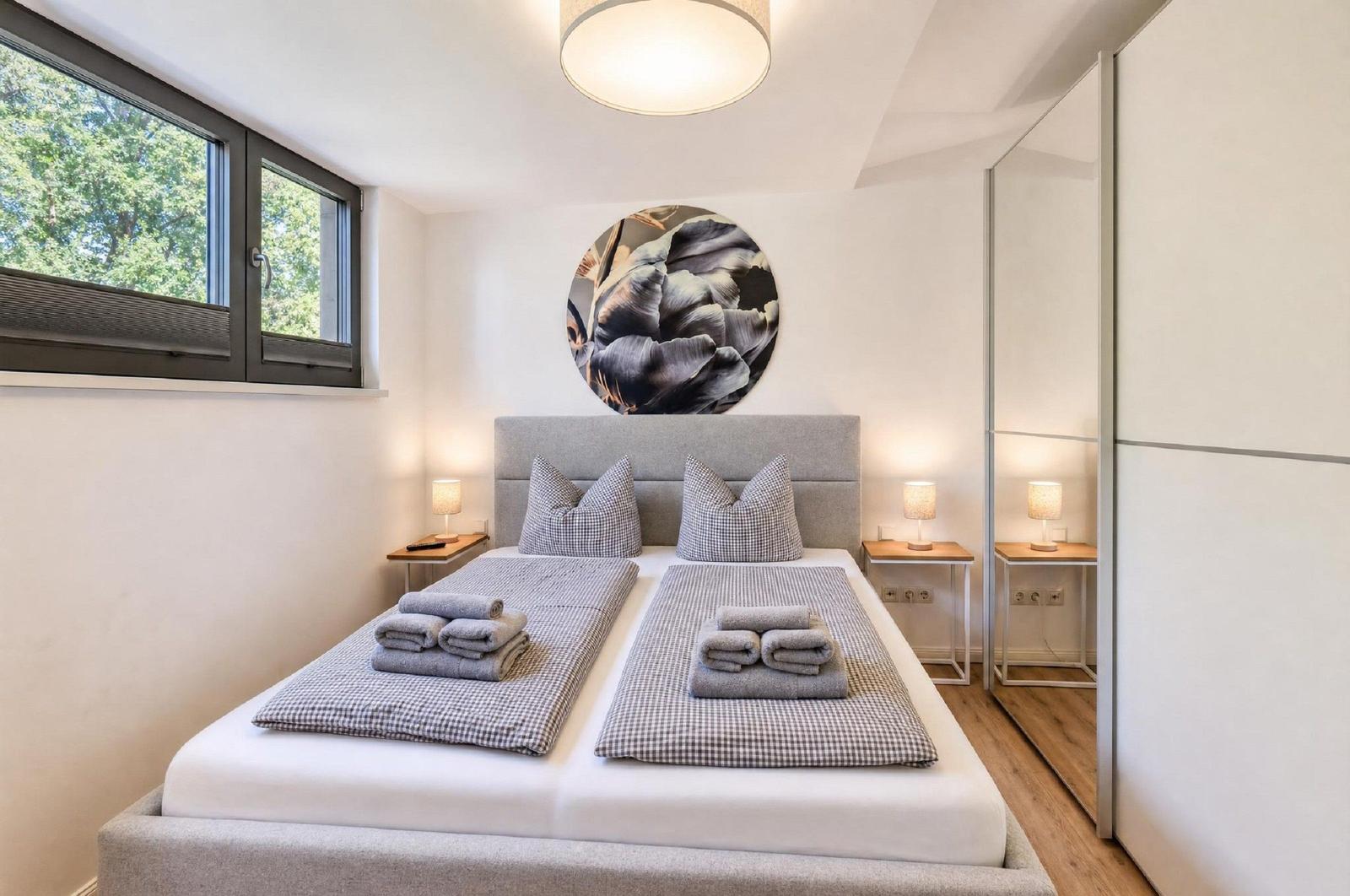 Schlafzimmer mit Doppelbett, zwei Nachttischen und Fenster mit Blick auf Bäume.
