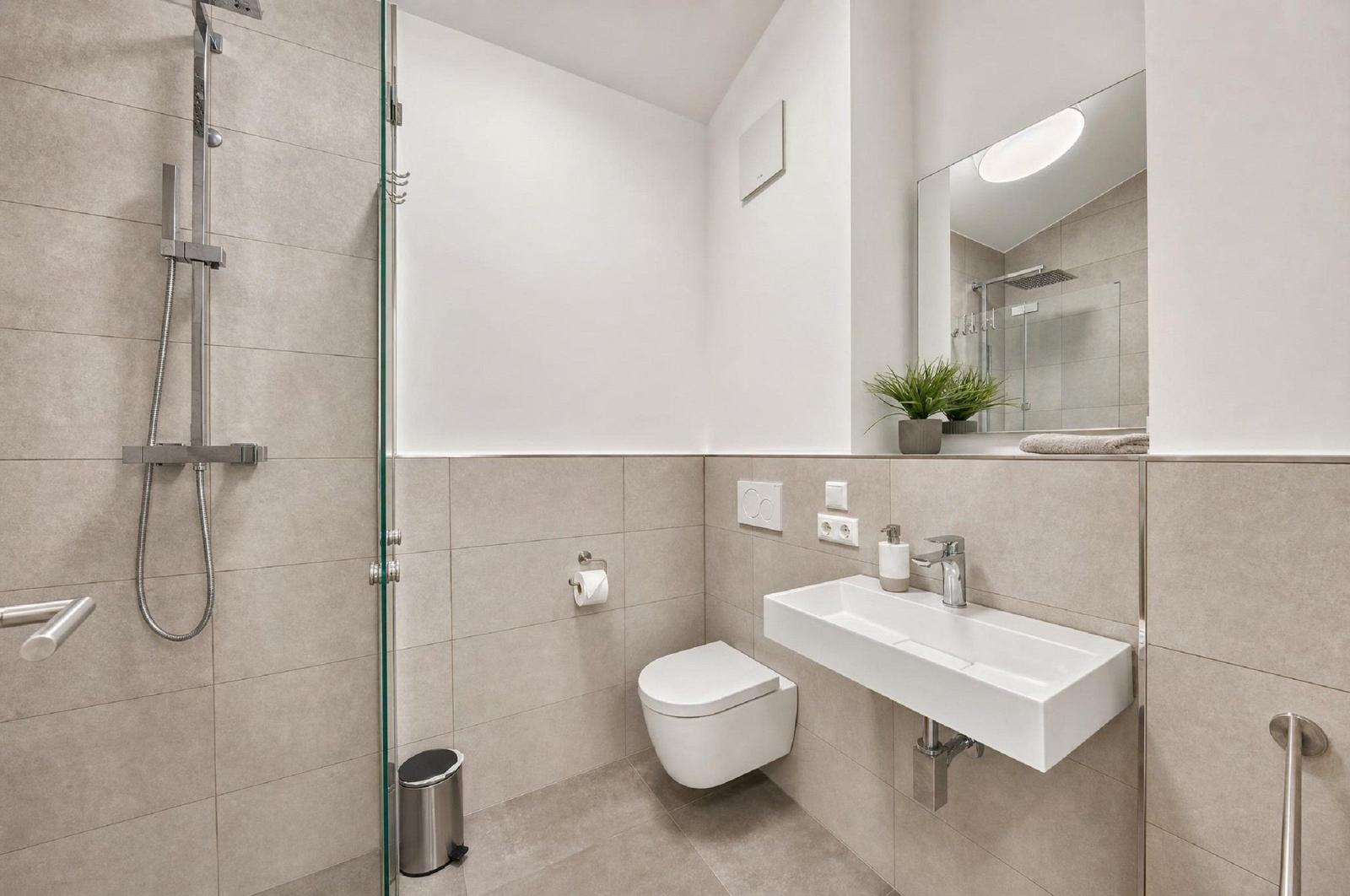Moderne Dusche mit Glaswand, WC und Waschbecken mit Spiegel.