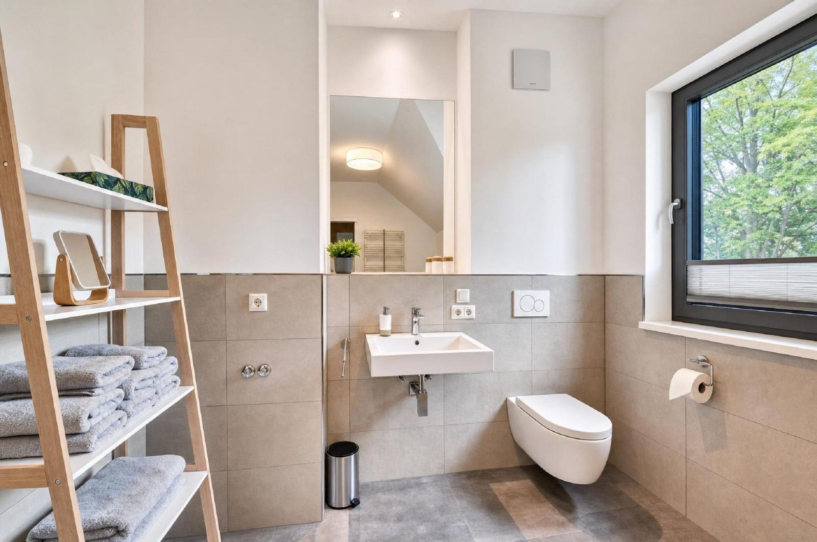 Badezimmer mit Waschbecken, Toilette und Fenster mit Blick auf Bäume.