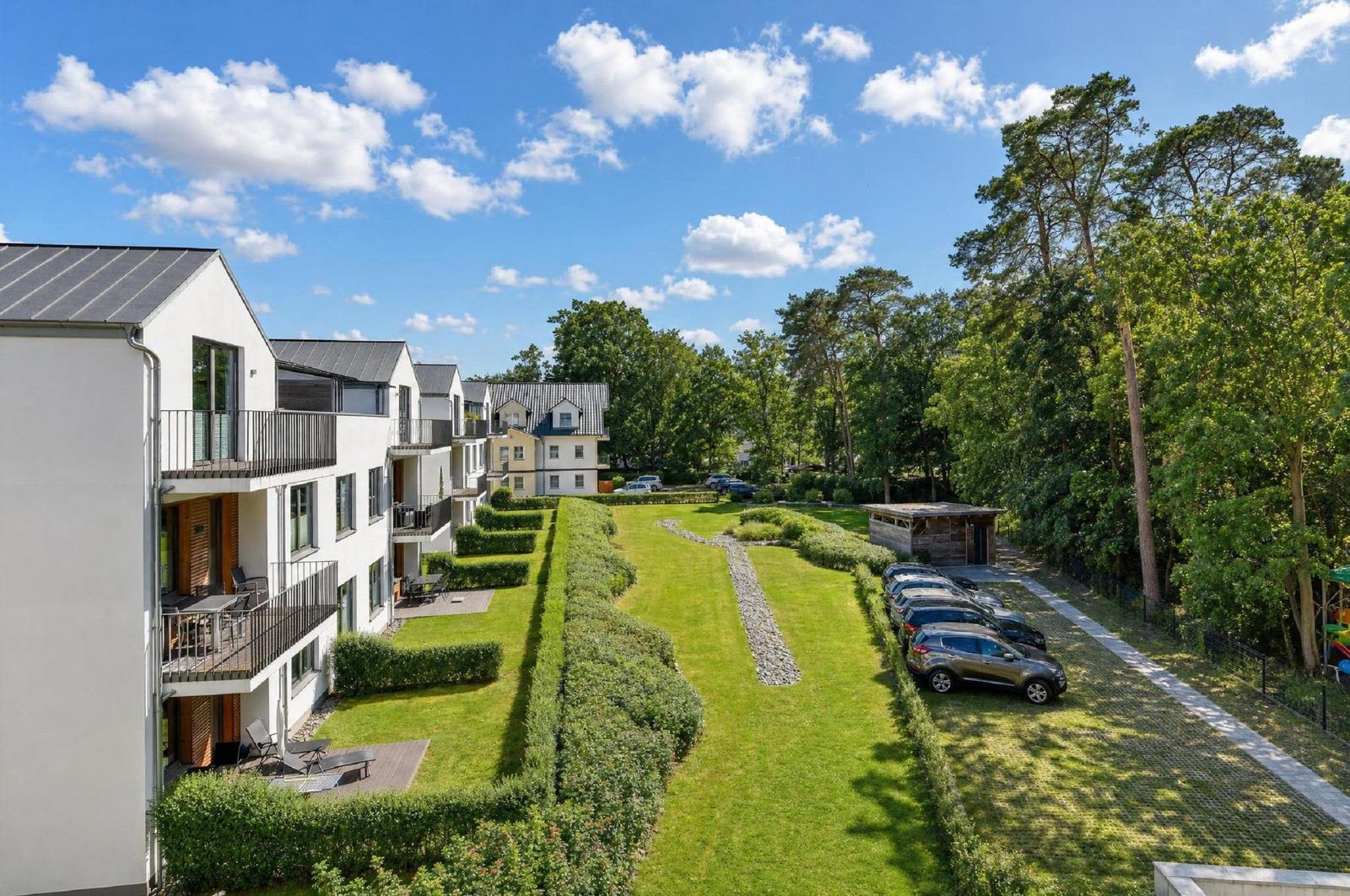 Moderne Apartments mit Balkonen, grüner Rasenfläche und Parkplatz in Waldnähe.