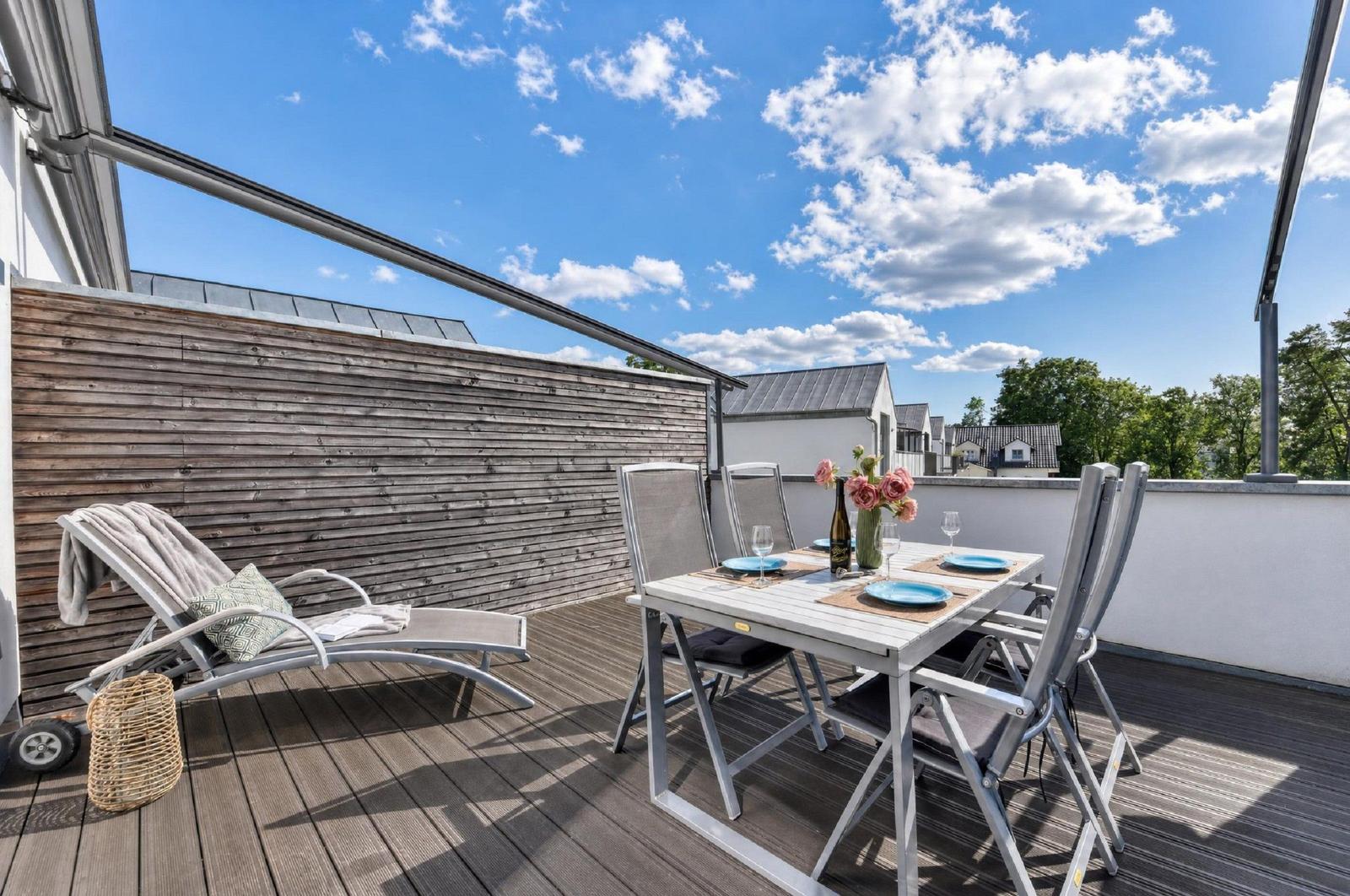 Terrasse mit Loungemöbeln und Esstisch unter blauem Himmel.