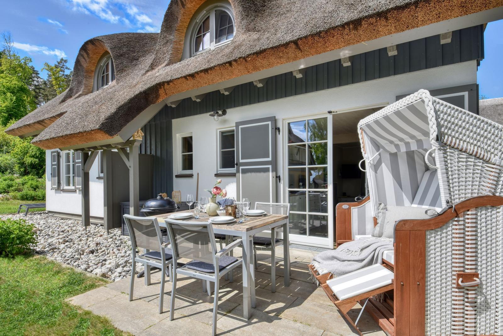 House with thatched roof, terrace with table, chairs, and beach chair.