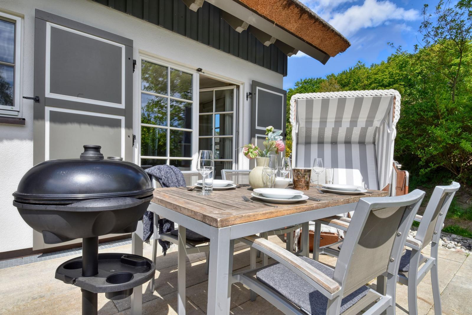 Terrace with table, chairs, grill, and beach chair. House with windows and roof.