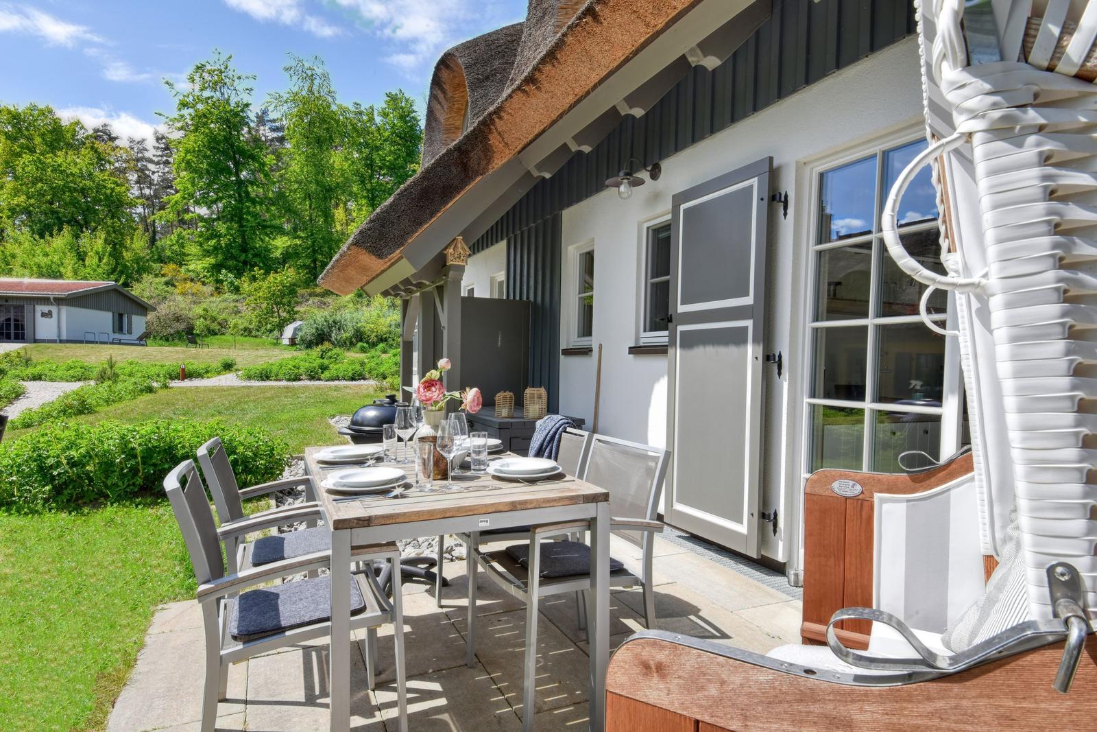 Terrace with table, chairs, and grill. Backyard with green areas and forest.