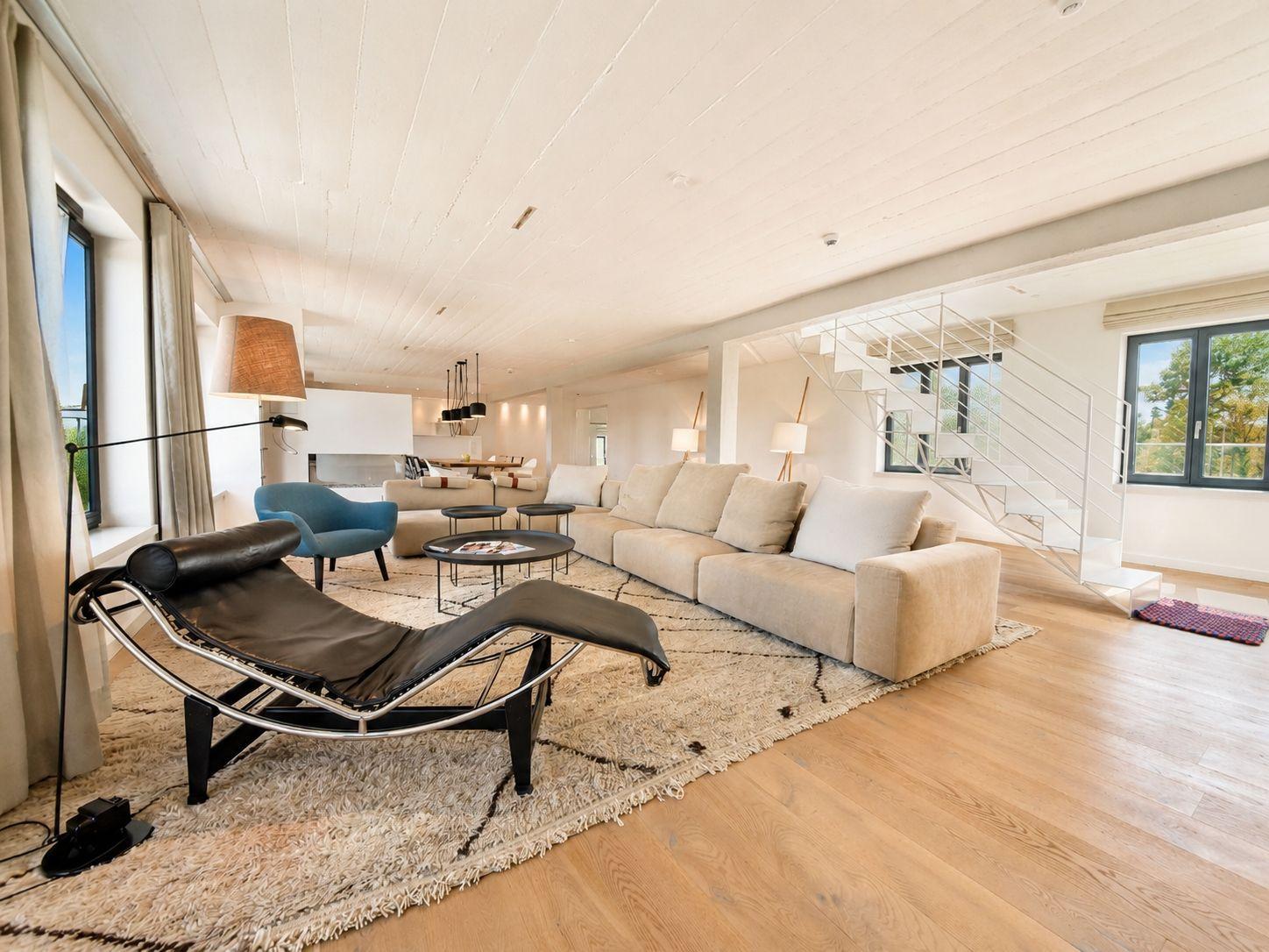 Wohnzimmer mit Sofa, Liege und Holzboden. Treppe und Fenster sichtbar.